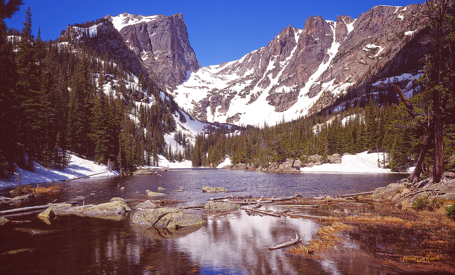 This is springtime at Dream Lake. The warm sun has melted the lake's winter covering of ice and snow. The grasses have begun...