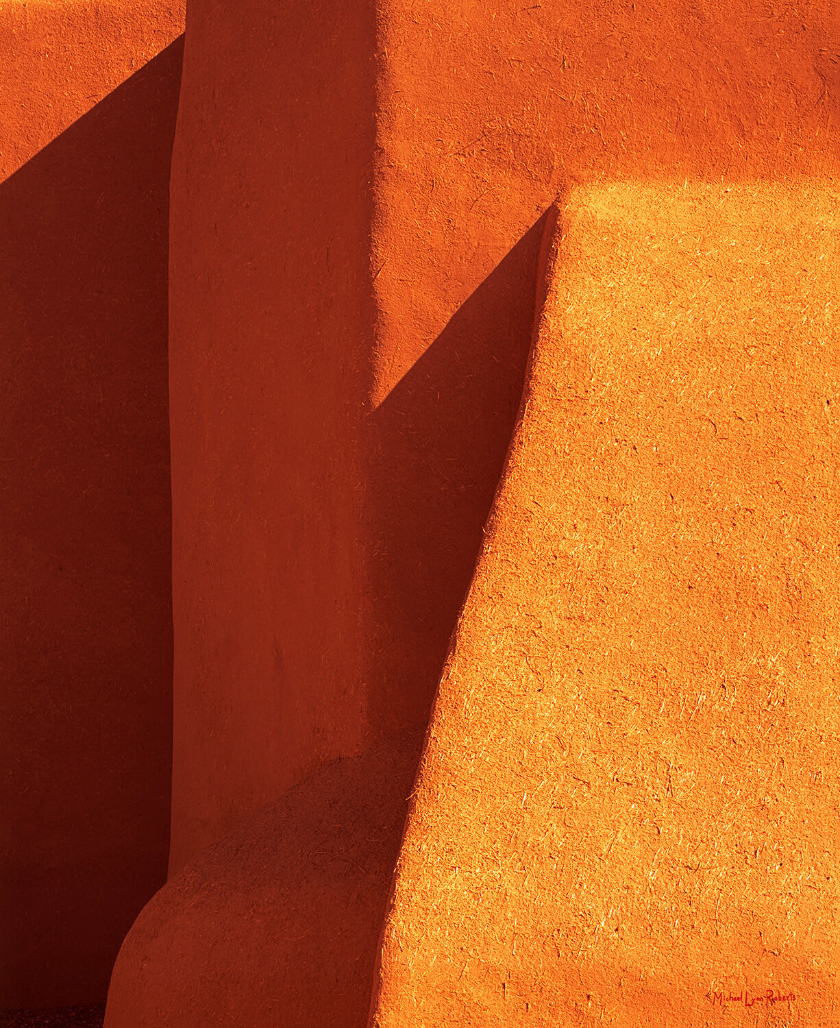 An abstract photographic closeup of light and shadow on a textured adobe wall of the St. Francis Mission in Rancho de Taos.